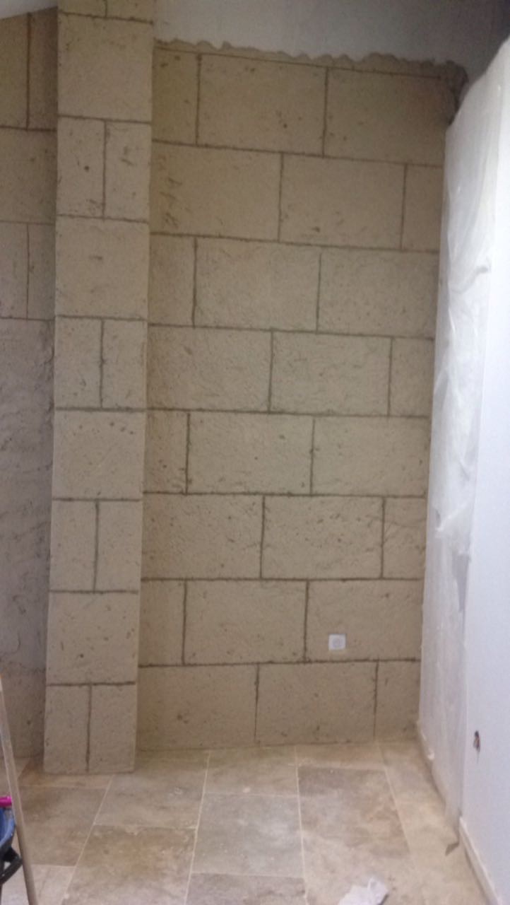 Cloison en blocs de béton montée dans une salle de bain en chantier, au-dessus d'un sol déjà carrelé en pierre
