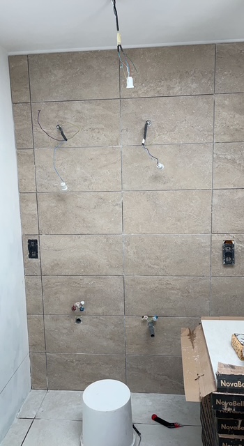 Mur de salle de bain habillé de faïence grand format imitation pierre, attentes de plomberie et fils électriques encore apparents