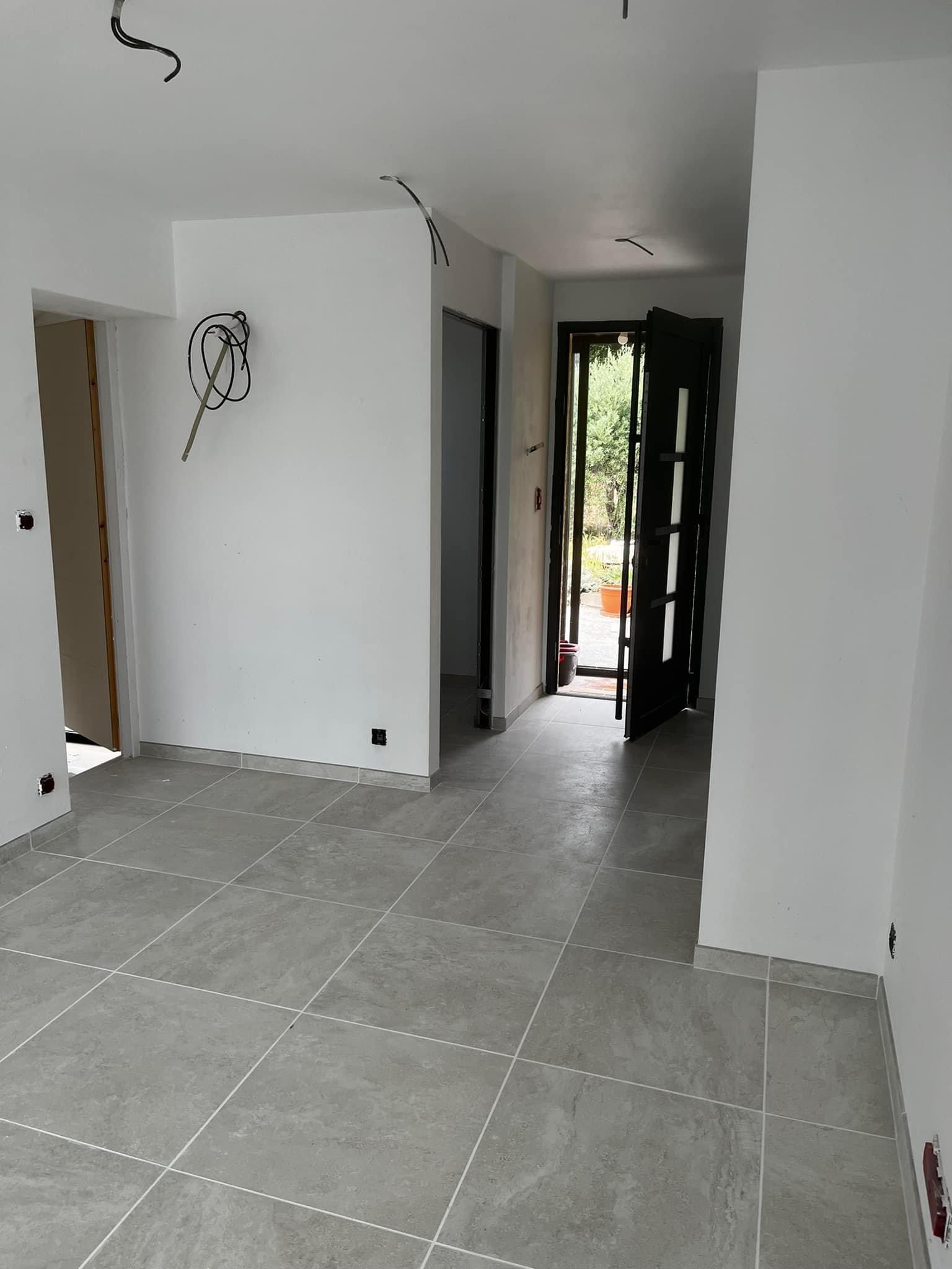 Sol en carrelage grand format gris posé dans une pièce rénovée, les joints alignés d'un mur à l'autre et les coupes ajustées le long des cloisons
